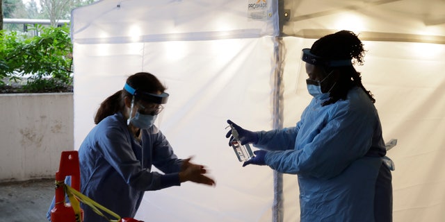 Nurses at a drive-up coronavirus testing station set up by the University of Washington Medical Center sanitize their hands after taking a nose swab sample from a person in a car Friday, March 13, 2020, in Seattle.  (AP Photo/Ted S. Warren)