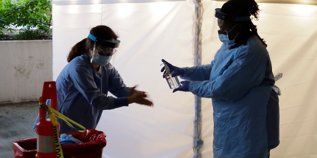 Nurses at a drive-up coronavirus testing station set up by the University of Washington Medical Center sanitize their hands after taking a nose swab sample from a person in a car Friday, March 13, 2020, in Seattle. (AP Photo/Ted S. Warren)