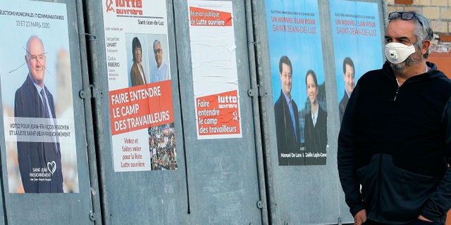 A masked man walks past posters advertising the upcoming local elections, in Saint Jean de Luz, southwestern France, on Saturday 14 March 2020. Authorities fear that the new coronavirus and the COVID-19 disease it causes will scare people away from polling stations and will have a serious impact on the turnout. (Photo AP / Bob Edme)