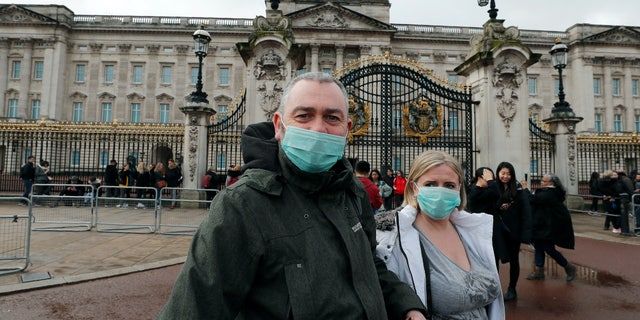 A couple wears a face mask to protect against the Coronavirus outbreak as they visit Buckingham Palace in London, Saturday, March 14, 2020. For most people, the new coronavirus causes only mild or moderate symptoms, such as fever and cough. For some, especially older adults and people with existing health problems, it can cause more severe illness, including pneumonia.(AP Photo/Frank Augstein)