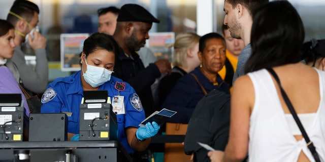 A Transportation Security Administration agent hands a passport back to a traveler as she screens travelers, at a checkpoint inside an airline terminal at John F. Kennedy Airport in New York. (AP Photo/Kathy Willens, File).