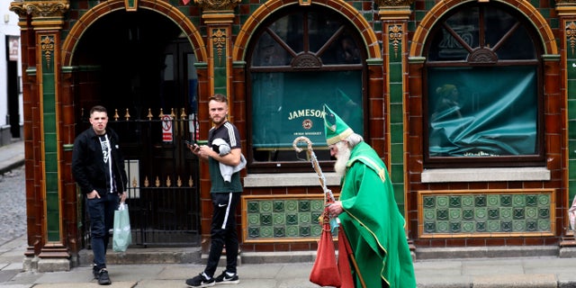 A man dressed as St Patrick walks past a closed bar in Dublin city centre, Monday, March, 16, 2020. All pubs in the Republic of Ireland closed late Sunday to try and tackle the spread of Covid-19. For most people, the new coronavirus causes only mild or moderate symptoms. For some it can cause more severe illness, especially in older adults and people with existing health problems.(AP Photo/Peter Morrison)