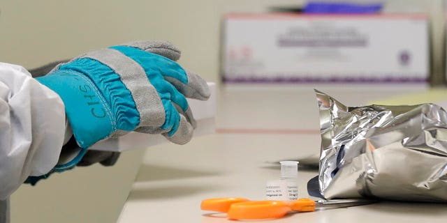 Pharmacist Michael Witte wears heavy gloves as he opens a frozen package of the potential vaccine for COVID-19, the disease caused by the new coronavirus, on the first day of a first-stage safety study clinical trial, Monday, March 16, 2020, at the Kaiser Permanente Washington Health Research Institute in Seattle. (AP Photo/Ted S. Warren)