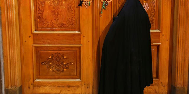A woman prays behind a closed door of Masoume shrine in the city of Qom, some 80 miles south of the capital Tehran, Iran, Monday, March 16, 2020.