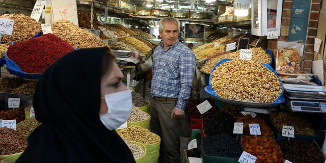 In this photo taken on Tuesday, March 17, 2020, a shopkeeper waits for customer as a woman wearing a face mask to help protect against the new coronavirus, walks at the Tehran's Grand Bazaar, Iran. (AP Photo/Vahid Salemi)