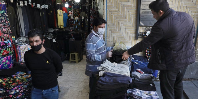 In this Tuesday photo, a shopkeeper wearing a face mask and gloves, to help protect against the new coronavirus, center, talks with his customer at the Tehran's Grand Bazaar, Iran. The new coronavirus ravaging Iran is cutting into celebrations marking the Persian New Year, known as Nowruz. (AP Photo/Vahid Salemi)