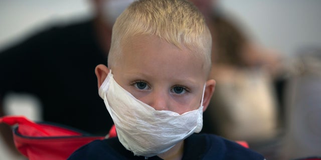 A boy wears a mask as he waits to travel from O.R.Tambo Airport in Johannesburg, South Africa, Thursday, March 19, 2020. As more African countries closed their borders, the coronavirus' local spread threatened to turn the continent of 1.3 billion people into an alarming new front for the pandemic.  (AP Photo/Denis Farrell)