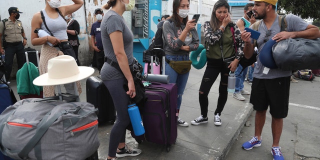 Tourists from the United States wait outside the closed Jorge Chavez International Airport for a member of the U.S. Embassy to escort them to a flight that will fly them back to the U.S., in Callao Peru, Friday, March 20, 2020, on the fifth day of a state of emergency decreed by the government to prevent the spread of the new coronavirus. (AP Photo/Martin Mejia)