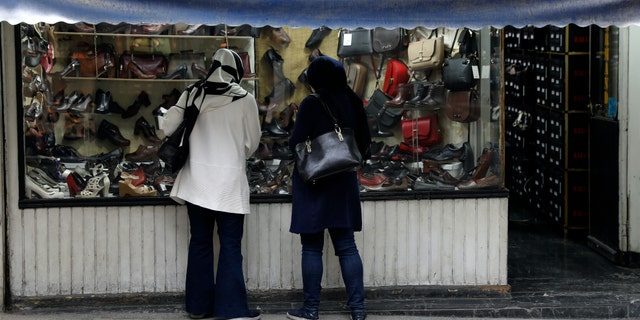 Two women look at shoes of a shop in a mostly empty street in a commercial district in downtown Tehran, Iran, Sunday, March 22, 2020. On Sunday, Iran imposed a two-week closure on major shopping malls and centers across the country to prevent spreading the new coronavirus. Pharmacies, supermarkets, groceries and bakeries will remain open. (AP Photo/Vahid Salemi)