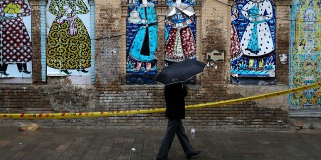 A man shelters from the rain with an umbrella as he walks past an old building decorated with a replica of Iranian old paintings in a mostly empty street in a commercial district in downtown Tehran, Iran, Sunday, March 22, 2020. On Sunday, Iran imposed a two-week closure on major shopping malls and centers across the country to prevent spreading the new coronavirus. Pharmacies, supermarkets, groceries and bakeries will remain open. (AP Photo/Vahid Salemi)