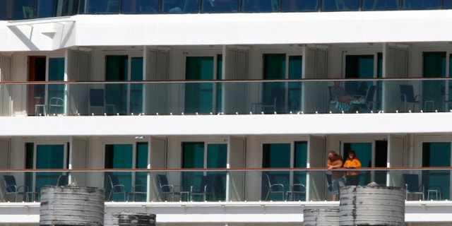 Two people look out from the Norwegian Jewel cruise ship in Honolulu on March 23. Passengers from the cruise ship that was turned away from other ports before arriving in Hawaii are being taken to Honolulu airport for chartered flights home. (AP Photo/Caleb Jones)