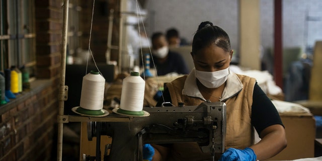 A woman sews high-quality face masks at a furniture factory in Eldorado Park, Johannesburg, Tuesday, March 24, 2020 in their fight against the coronavirus the day after it was announced that South Africa will go into a nationwide lockdown for 21 days from Thursday. (AP Photo/Shiraaz Mohamed)