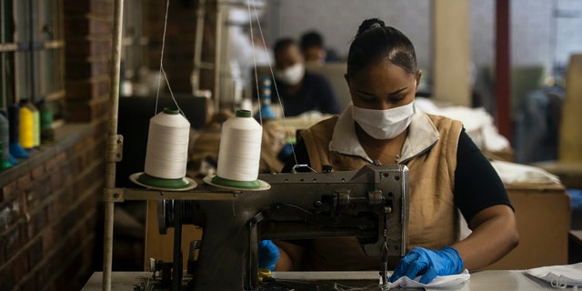 A woman sews high-quality face masks at a furniture factory in Eldorado Park, Johannesburg, Tuesday, March 24, 2020 in their fight against the coronavirus the day after it was announced that South Africa will go into a nationwide lockdown for 21 days from Thursday. (AP Photo/Shiraaz Mohamed)