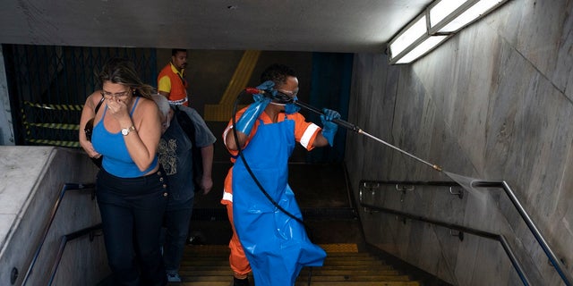 A city worker sprays disinfectant at the entrance of a metro station, which is open for service, in Rio de Janeiro, Brazil to help prevent the spread of the new coronavirus. (AP Photo/Leo Correa)