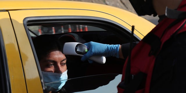 A firefighter checks the body temperature of a commuter at a toll gate, at the northern entrance to the city of Quito, Ecuador on Tuesday. Due to the worldwide spread of the new coronavirus, the government has declared a "health emergency," restricting movement to only those who provide basic services, enacting a curfew, and closing schools. (AP Photo/Dolores Ochoa)
