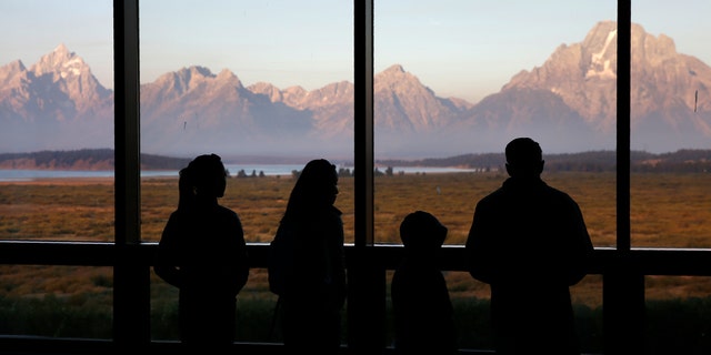 FILE - In this Aug. 28, 2016 file photo visitors watch the morning sun illuminate the Grand Tetons from within the Great Room at the Jackson Lake Lodge in Grand Teton National Park north of Jackson, Wyo.  (AP Photo/Brennan Linsley,File)