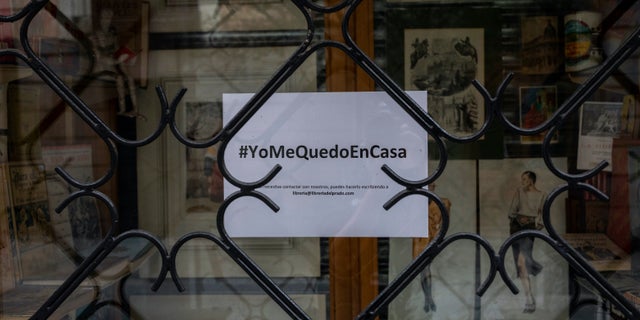 A poster reading in Spanish the hashtag "#IstayAtHome" hangs in windowshop of a closed shop in downtown Madrid, Spain, Tuesday, March 24, 2020. More than 1.5 billion around the world have been told to stay in their homes.