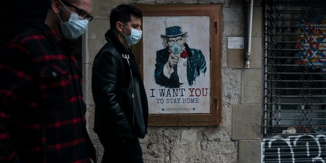 People walk past a poster that reads ‘I want you to stay home’, by artist TvBoy amid a lockdown in Barcelona, Spain, Tuesday, March 24, 2020. 