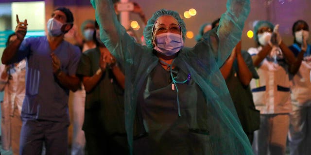 FILE: Health workers react as people applaud from their houses in support of the medical staff that are working on the COVID-19 virus outbreak at the Jimenez Diaz Foundation University hospital in Madrid, Spain. 