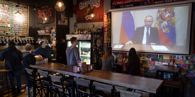 A few visitors and staff of the pub watching the broadcast of Russian President Vladimir Putin addresses Russian citizens on the State Television channels in Moscow, Russia, Wednesday, March 25, 2020. Putin has postponed a nationwide vote on proposed constitutional amendments that include a change that would allow him to seek another term in power. He also announced during a televised address to the nation that the government doesn't want Russians except those working in essential sectors to come to work next week. He said that stores, pharmacies and banks will stay open.