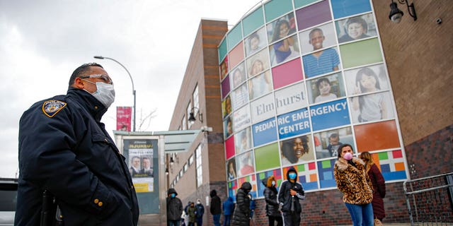 An NYPD officer wears personal protective equipment while maintaining order along a line to enter COVID-19 testing site at Elmhurst Hospital Center, Wednesday, March 25, 2020, in New York.