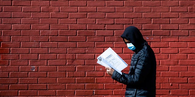 Terrell Bell, wearing a protective face mask, looks at a learning guide he picked up for his little sister at John H. Webster Elementary School in Philadelphia, Thursday, March 26, 2020. Gov. Tom Wolf’s administration reported more new coronavirus-related deaths in Pennsylvania on Wednesday. Residents are ordered to stay home, with few exceptions. (AP Photo/Matt Rourke)