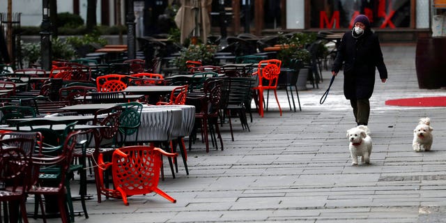A woman walks with dogs in a deserted street amid the coronavirus outbreak in downtown Belgrade, Serbia, Thursday, March 26, 2020.