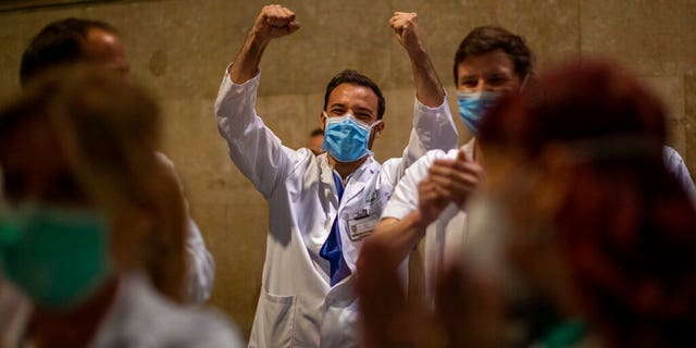 Health workers react as people applaud from their houses in support of the medical staff that are working on the COVID-19 virus outbreak at the main gate of the Hospital Clinic in Barcelona, Spain, Thursday, March 26, 2020.