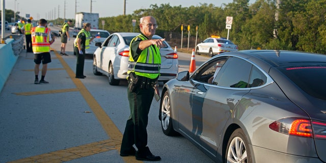 In this photo provided by the Florida Keys News Bureau, Monroe County Sheriff’s Office Col. Lou Caputo directs a driver wanting to continue down the Florida Keys Overseas Highway near Key Largo, Fla. Friday, March 27, 2020. The Keys have been temporarily closed to visitors since March 22, because of the coronavirus crisis. Keys officials decided to established the checkpoint Friday to further lessen the threat of virus transmission to people in the subtropical island chain.