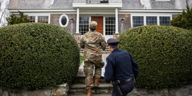 Rhode Island Air National Guard Sgt. William Randall, left, and Westerly police Officer Howard Mills approach a home in Westerly, R.I., while looking for New York license plates in driveways to inform them of self quarantine orders, March 28, 2020. (Associated Press)