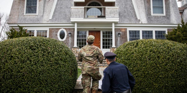 Rhode Island Air National Guard Sgt. William Randall, left, and Westerly police Officer Howard Mills approach a home in Westerly, R.I., while looking for New York license plates in driveways to inform them of self quarantine orders, March 28, 2020. (Associated Press)