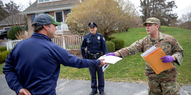 Rhode Island Air National Guard TSgt. William Randall, right, handing out an information sheet to a man self-quarantining at his home in Westerly, R.I.
