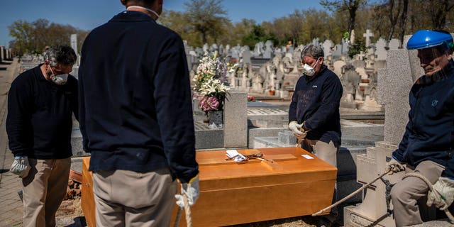 Undertakers take a moment while a priest and family, not seen, pray during the burial of an elderly victim of the COVID-19 at the Almudena cemetery in Madrid, Spain, Saturday March 28, 2020. In Spain, where stay-at-home restrictions have been in place for nearly two weeks, the official number of deaths is increasing daily. The new coronavirus causes mild or moderate symptoms for most people, but for some, especially older adults and people with existing health problems, it can cause more severe illness or death. (AP Photo/Olmo Calvo)
