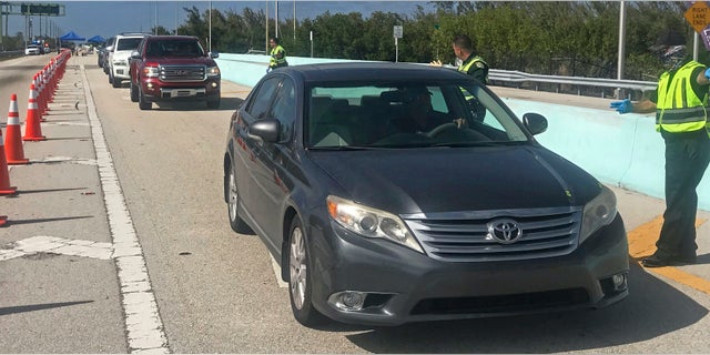 In this photo provided by the Florida Keys News Bureau, Monroe County Sheriff's Office Col. Lou Caputo, right, directs a driver wanting to continue down the Florida Keys Overseas Highway near Key Largo, Fla. Saturday, March 28, 2020. The Keys have been temporarily closed to visitors since March 22, because of the coronavirus crisis. Keys officials decided to established the checkpoint Friday, March 27, to further lessen the threat of virus transmission to people in the subtropical island chain. (Andy Newman/Florida Keys News Bureau via AP)