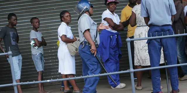 Zimbabwean police urge people to practice social distancing while in a queue to enter a supermarket in Harare, Zimbabwe, Monday, March 30, 2020. Zimbabwe went into lockdown for 21 days in an effort to curb the spread of the coronavirus. The new coronavirus causes mild or moderate symptoms for most people, but for some, especially older adults and people with existing health problems, it can cause more severe illness or death. (AP Photo/Tsvangirayi Mukwazhi)