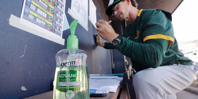 Oakland Athletics minor league manager Scott Steinmann fills-out a line-up in the MLB team's dugout next to a bottle of hand sanitizer before a spring training baseball game against the Seattle Mariners Saturday, March 7, 2020, in Peoria, Ariz. (AP Photo/Elaine Thompson)