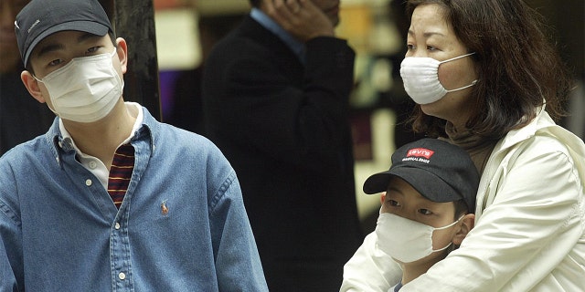 A family wears masks on a street in the Central business district of Hong Kong as the SARS outbreak grips the territory on March 24, 2003. (Photo by Peter PARKS / AFP) (Photo by PETER PARKS/AFP via Getty Images)