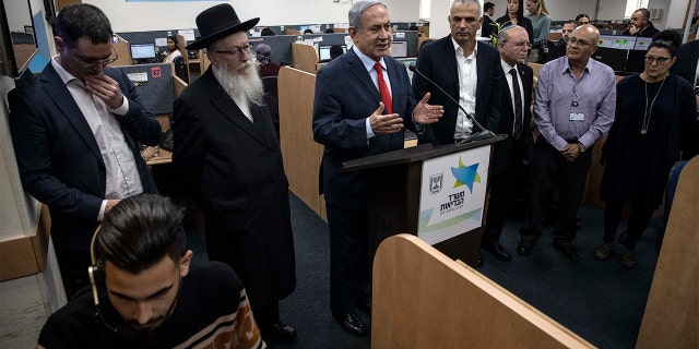 Israeli Prime Minister Benjamin Netanyahu, center, and Israeli Health Minister Yaakov Litzman, third left, speak during during their visit to the coronavirus outbreak central response unit at the Israeli Ministry of Health, in Kiryat Malachi, Israel, Sunday. (AP Photo/Tsafrir Abayov)