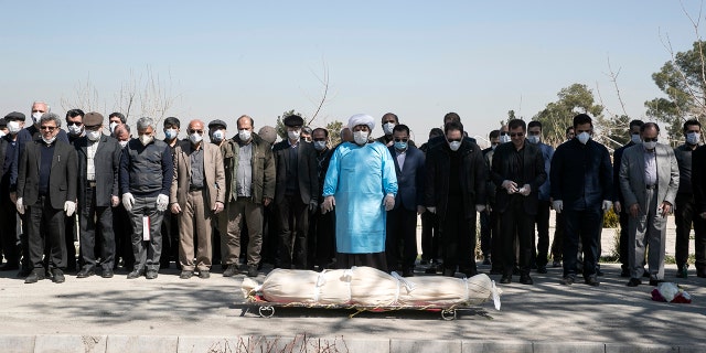 Mourners wearing face masks and gloves pray over the body of former politburo official in the Revolutionary Guard Farzad Tazari, who died Monday after being infected with the new coronavirus, at the Behesht-e-Zahra cemetery just outside Tehran, Iran, Tuesday. (Mahmood Hosseini/Tasnim News Agency via AP)