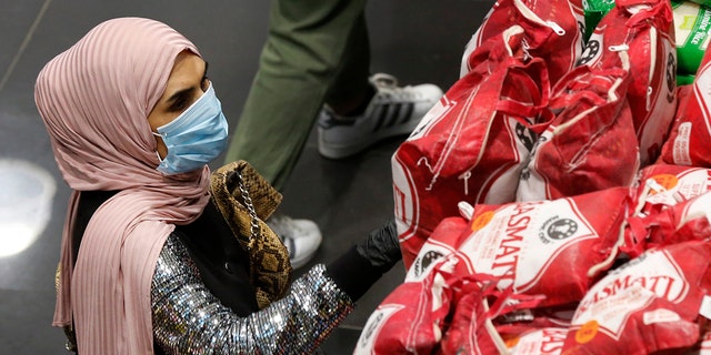 A woman wears a mask and gloves, as she checks products at a supermarket as people begin to stock up on provisions, in Beirut, Lebanon, Wednesday. (AP Photo/Hussein Malla)