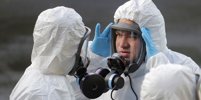 A worker from a Servpro disaster recovery team wearing a protective suit and respirator adjusts his mask before entering the Life Care Center in Kirkland, Wash. to begin cleaning and disinfecting the facility, Wednesday, March 11, 2020, near Seattle. 