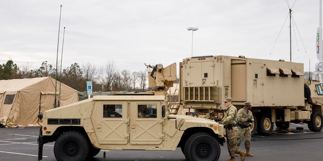 Soldiers with a security unit guard the perimeter as members of the National Guard set up tents to be used for coronavirus testing, Saturday, March 21, 2020, in a parking lot for FedEx Field in Landover, Md., outside of Washington. (AP Photo/Jacquelyn Martin)