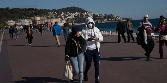 People wearing masks walk along Nice's Promenade des Anglais in Nice, southern France, Sunday, March 15, 2020. (AP Photo/Daniel Cole)