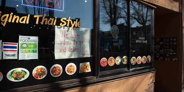 A sign indicating take out and delivery services are available is displayed in a window of a restaurant in the University District of Seattle, Washington on March 18.