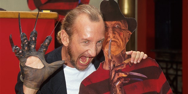 Actor Robert Englund posing with a cardboard cutout of character Freddy Krueger from his film series 'Nightmare on Elm Street.'