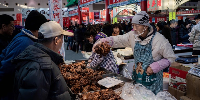 A vendor sells meat to customers at a market in Beijing on Jan. 15.