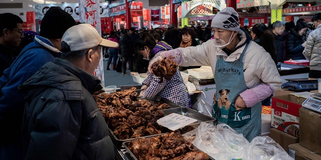 A vendor sells meat to customers at a market in Beijing on Jan. 15.