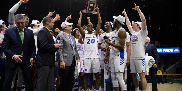 Hofstra guard Jalen Ray (20) and others raise the trophy after defeating Northeastern in an NCAA college basketball game for the championship of the Colonial Athletic Association men's tournament Tuesday, March 10, 2020, in Washington. Hofstra won 70-61. (AP Photo/Nick Wass)
