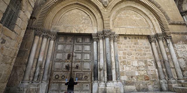 A woman prays in front of the Church of the Holy Sepulchre in the Old City of Jerusalem after the city was closed to non-residents as a measure to contain the spread of the novel coronavirus, on March 30, 2020.