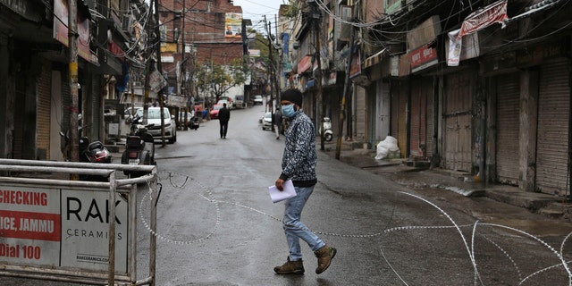 An Indian man wearing a mask walks past a barbed wire erected by authorities as part of enforcing a lockdown as a precautionary measure against COVID-19 in Jammu, India, Tuesday, March 24, 2020.